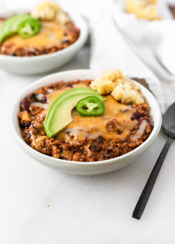 chipotle apple turkey chili topped with cheese, avocado and jalapeño in a grey bowl.