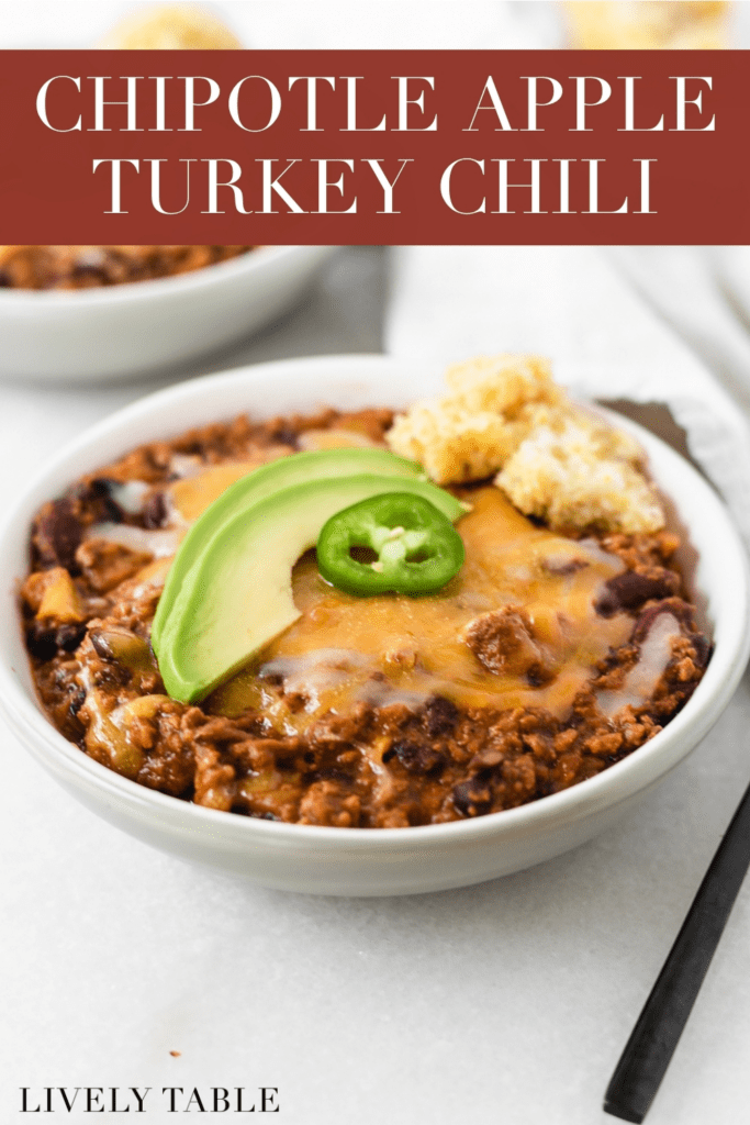 chipotle apple turkey chili topped with cheese, avocado and jalapeño in a grey bowl with text overlay.