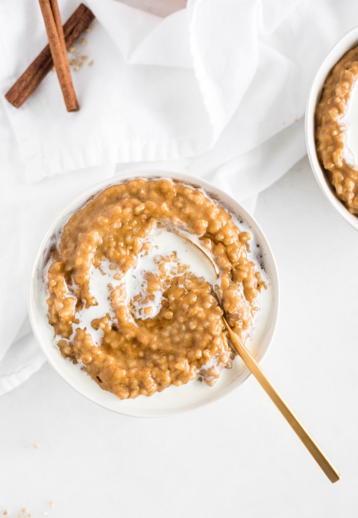 overhead view of a bowl of maple pumpkin spice oatmeal with milk on top and a gold spoon stuck in it.