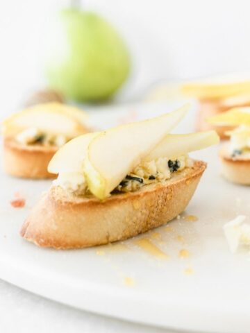 pear blue cheese crostini drizzled with honey on a white marble board.