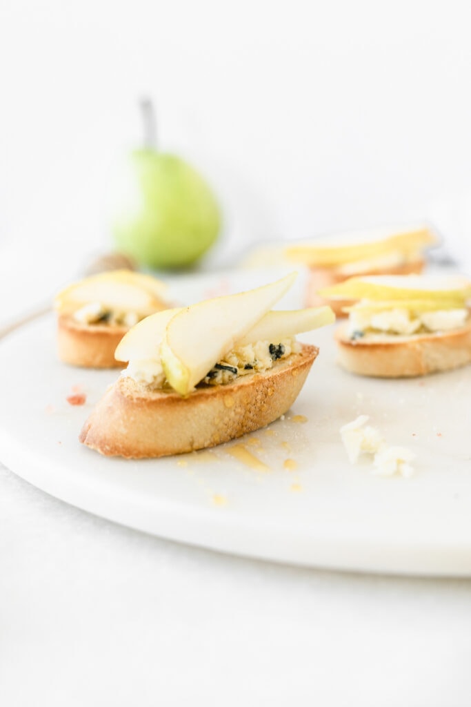 pear blue cheese crostini drizzled with honey on a white marble board.