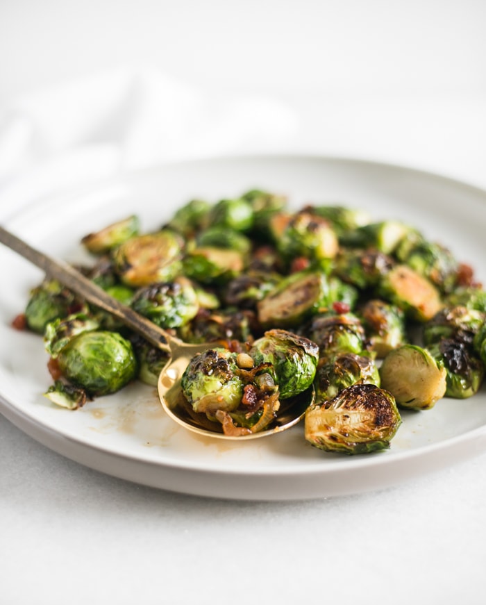 Bourbon Brown Sugar Roasted Brussels Sprouts with Bacon on a plate with a gold spoon in them.