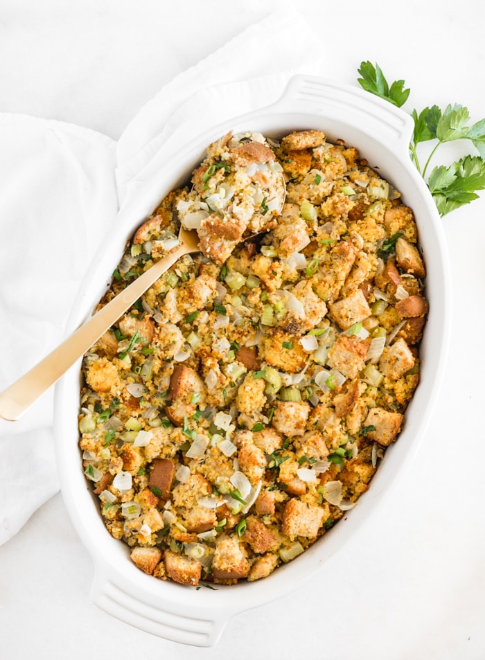 overhead view of southern cornbread stuffing in a white oval baking dish with a gold spoon in it.