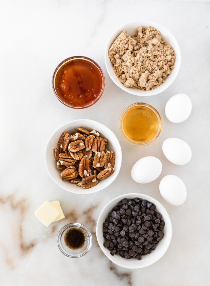 overhead view of ingredients needed to make chocolate bourbon pecan pie on a white marble background.
