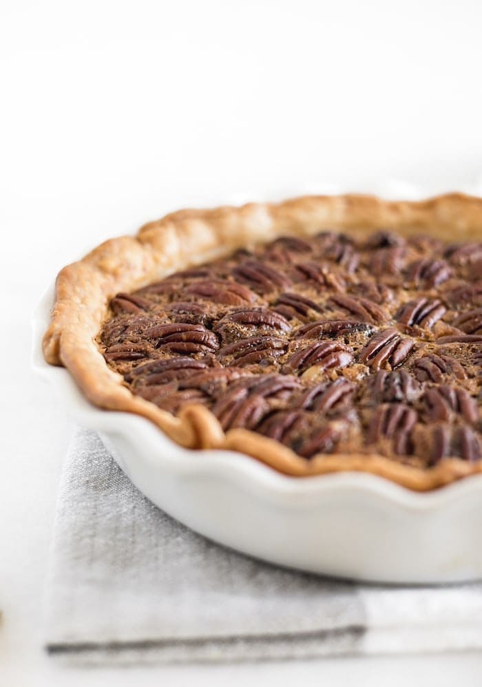 closeup of whole chocolate bourbon pecan pie on a white pie dish.