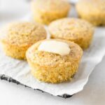 gluten-free polenta cornbread muffin with butter on top on a parchment lined wire rack.