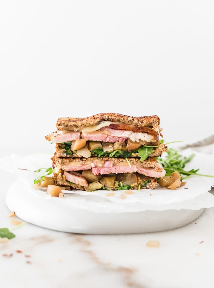 ham and gouda sandwich with spicy apple chutney and arugula cut in half and stacked on a plate.