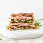ham and gouda sandwich with spicy apple chutney and arugula cut in half and stacked on a plate.