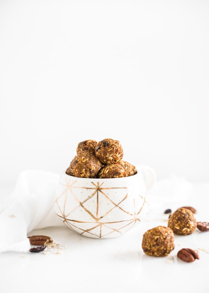 healthy pumpkin protein balls with pecans and cranberries stacked in a white and gold mug.