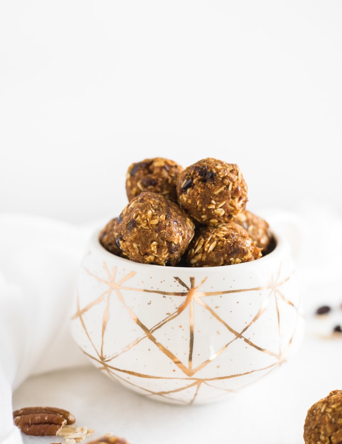 healthy pumpkin protein balls with pecans and cranberries stacked in a white and gold mug.