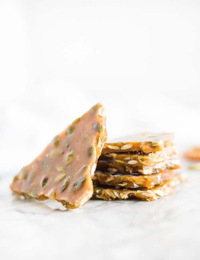 pieces of maple bourbon pumpkin seed brittle stacked on a white background.