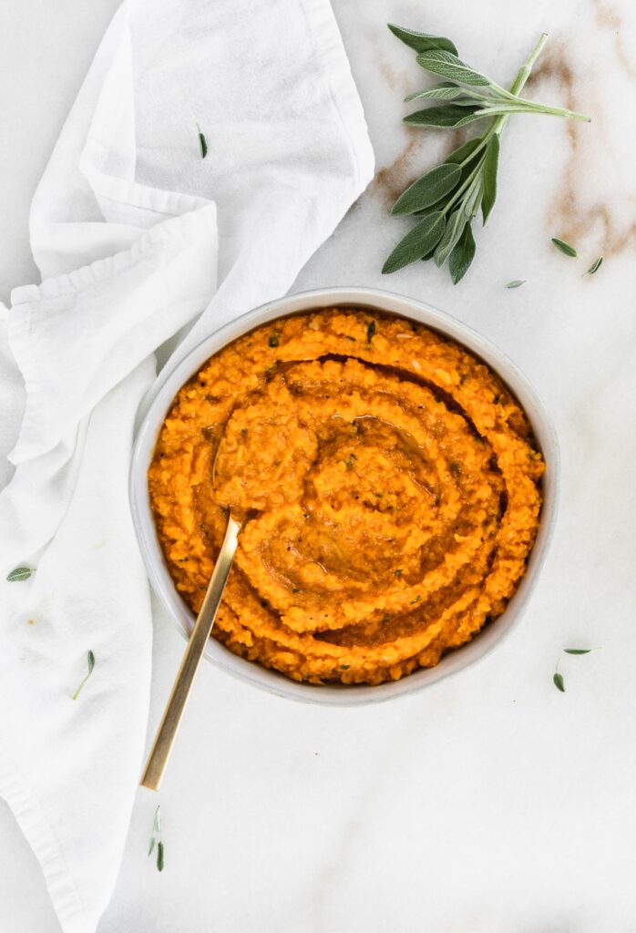 brown butter sage mashed sweet potatoes in a bowl with melted butter on top and a gold spoon in them.