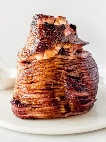 maple brown sugar glazed ham standing on the cut side on a white marble board.