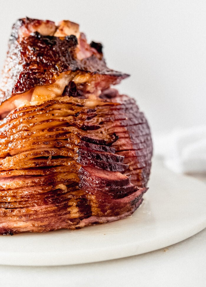 closeup of maple brown sugar glazed ham standing on the cut side on a white marble board.