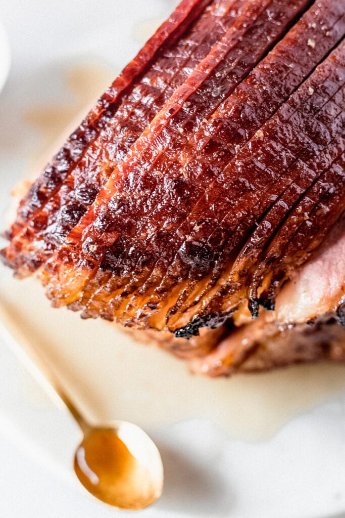 gold spoon pouring maple brown sugar glaze over a spiral ham.