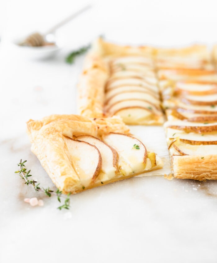 closeup of a piece of pear puff pastry tart surrounded by thyme and sea salt.