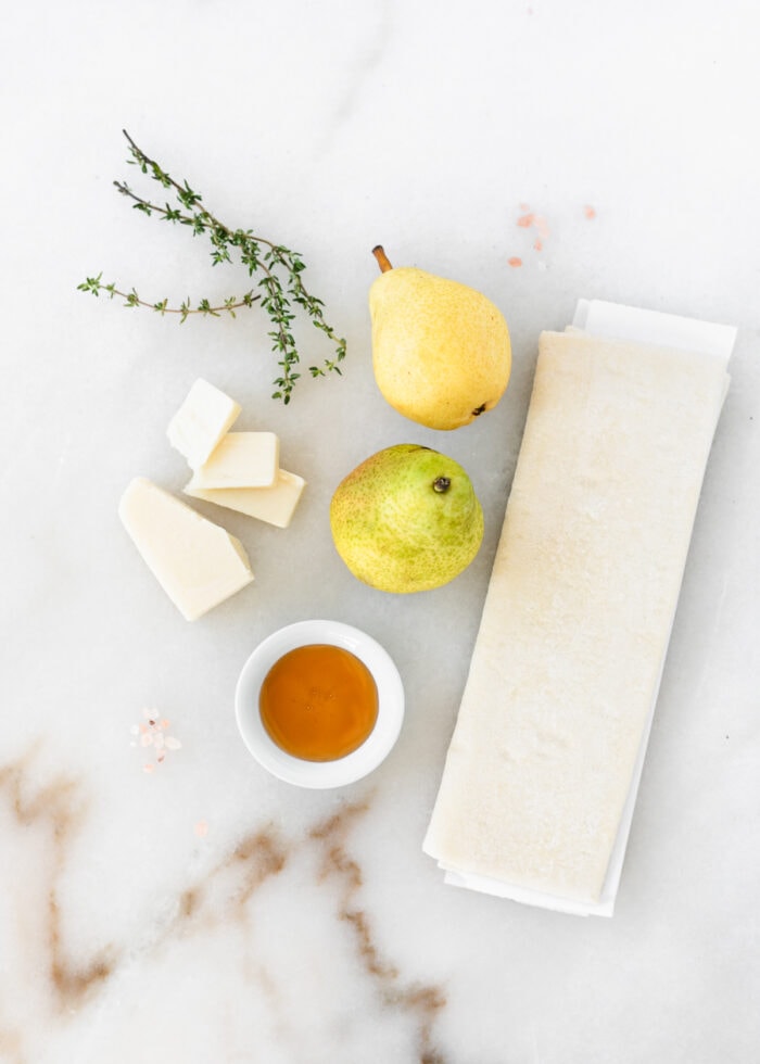 overhead view of ingredients needed to make Pear Gruyere Puff Pastry Tart on a white marble background.