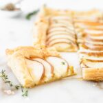 closeup of a piece of pear puff pastry tart surrounded by thyme and sea salt.