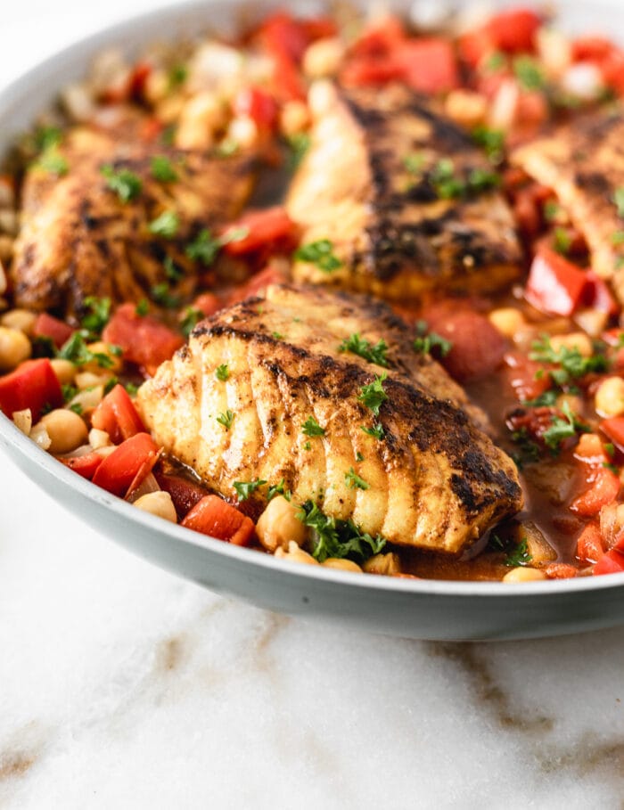 closeup of moroccan cod with stewed chickpeas and tomatoes in a skillet.