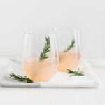 two grapefruit prosecco cocktails garnished with rosemary in stemless wine glasses.