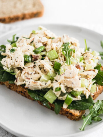 no mayo orange poppy seed chicken salad on a piece of bread with greens on a white plate.