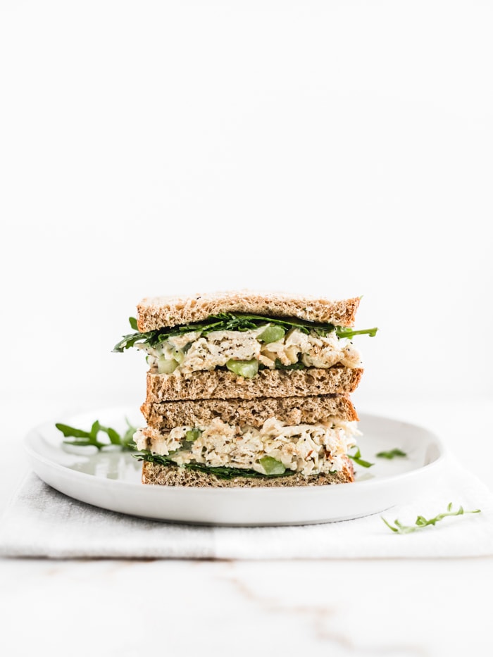 two halves of a chicken salad sandwich stacked on top of each other on a white plate.