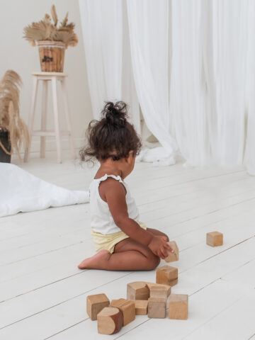 baby on a white wood floor playing with wood blocks.