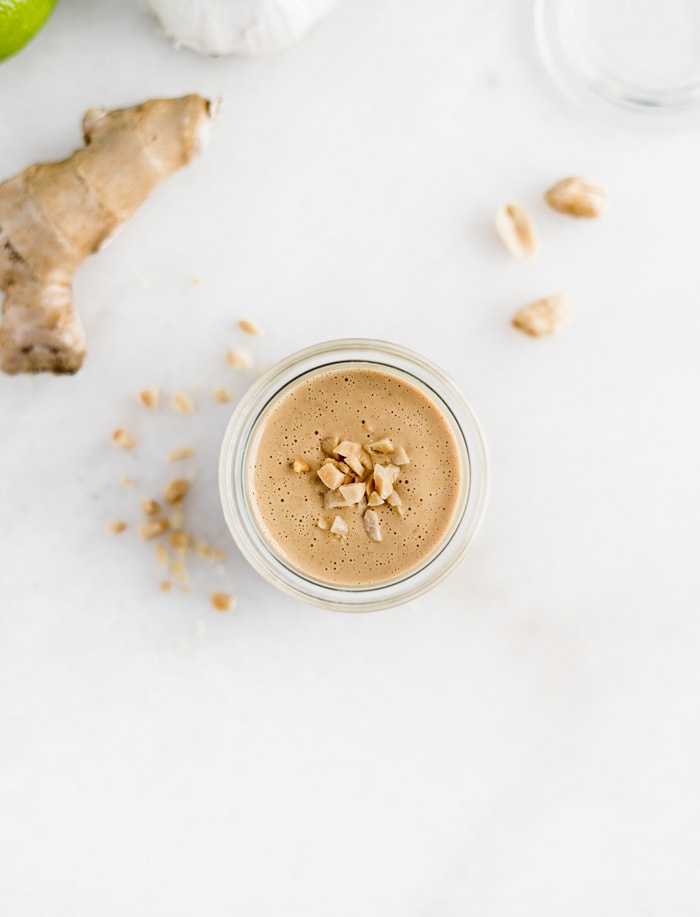 overhead view of all purpose thai peanut sauce in a glass jar with chopped peanuts on top.