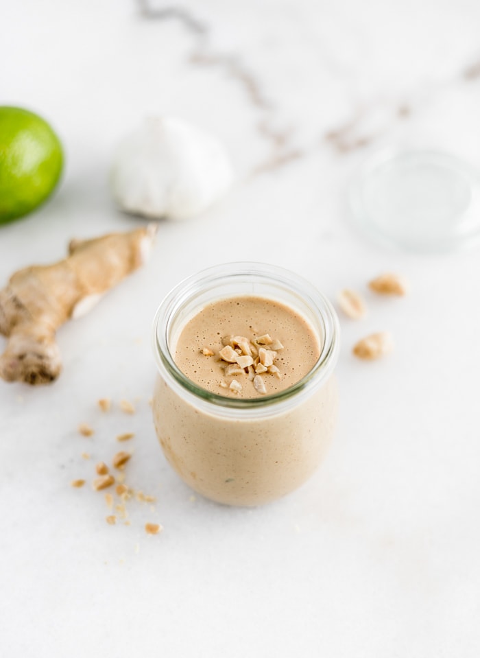 all purpose thai peanut sauce in a glass jar with ginger, lime and garlic behind it.