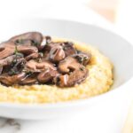 closeup of red wine mushrooms on top of parmesan polenta in a white bowl.