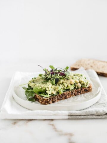 Vegan chickpea avocado salad on a piece of toast with mixed greens.