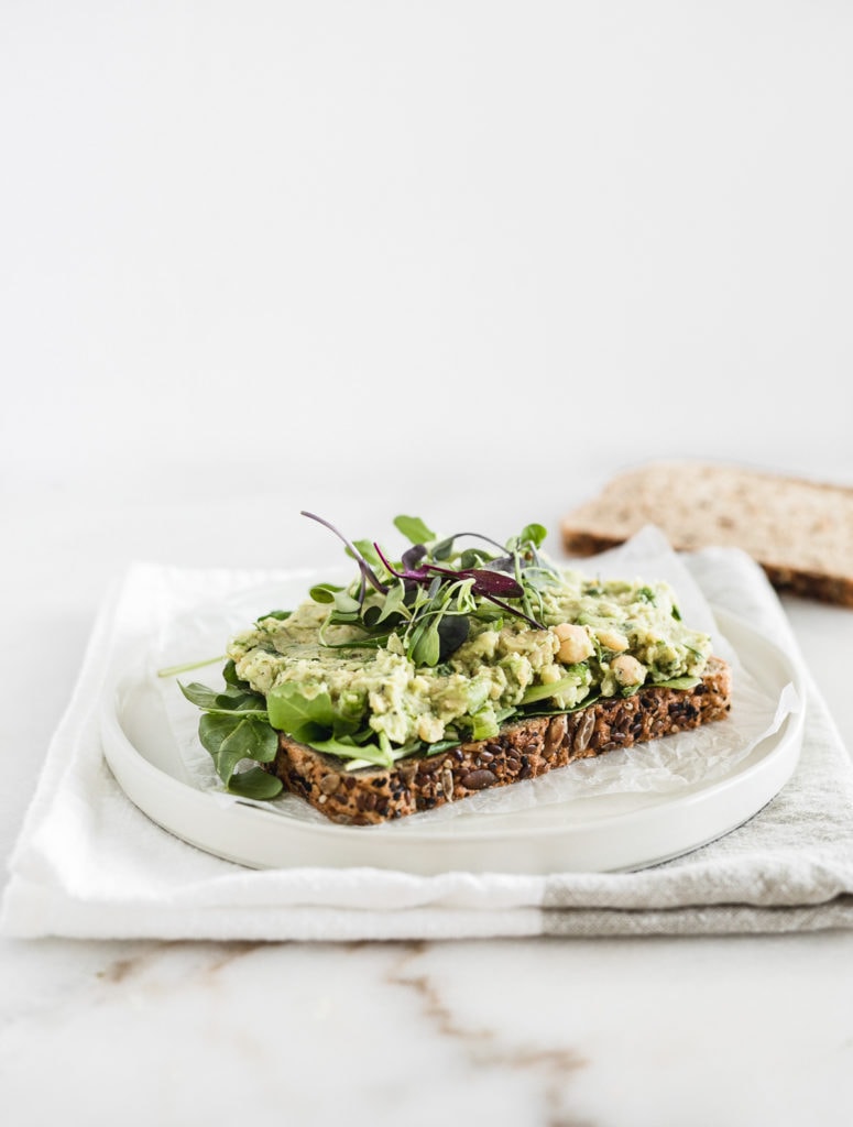 Vegan chickpea avocado salad on a piece of toast with mixed greens.