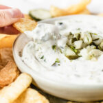 potato chip dipping into a small bowl of dill pickle dip.