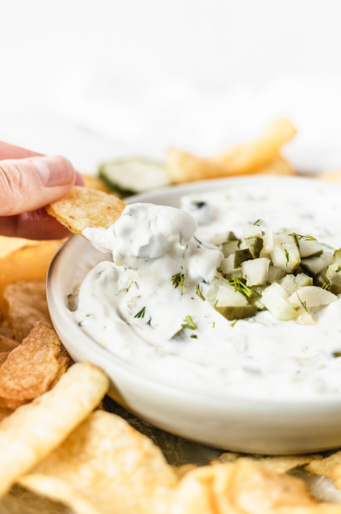 potato chip dipping into a small bowl of dill pickle dip.
