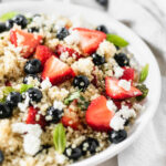 Closeup of a Red White and Blue Berry Quinoa Salad in a white bowl.