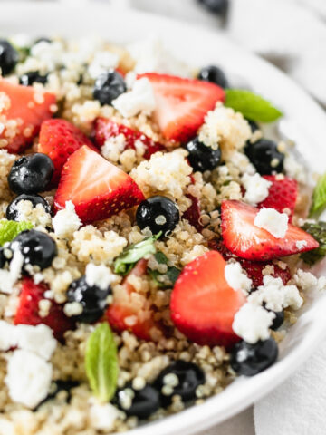 Closeup of a Red White and Blue Berry Quinoa Salad in a white bowl.