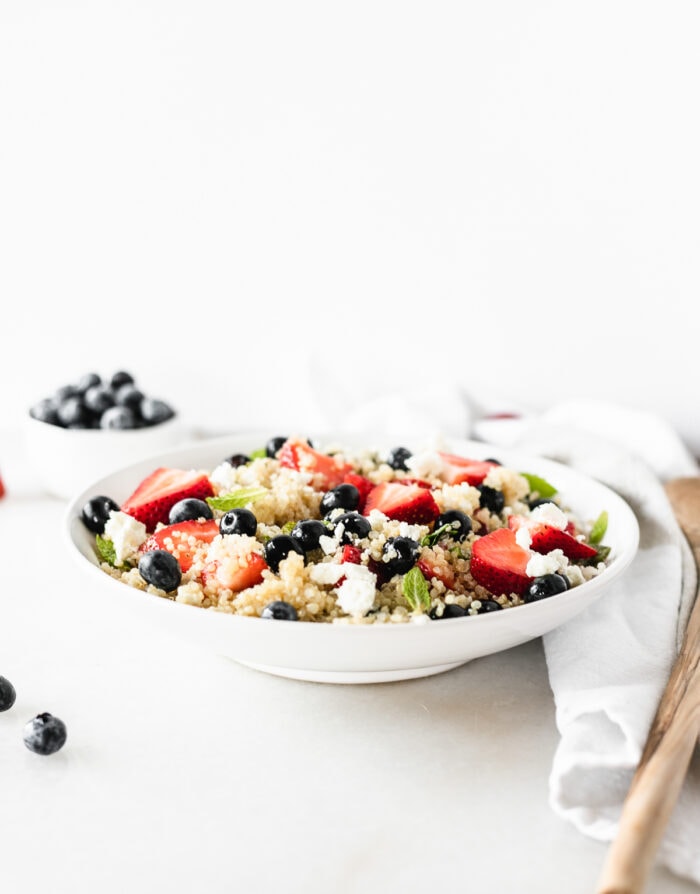 Red White and Blue Berry Quinoa Salad in a white bowl with a small bowl of blueberries in the background.