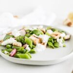 snap pea salad with burrata, sourdough croutons, and lemon vinaigrette on a white plate.