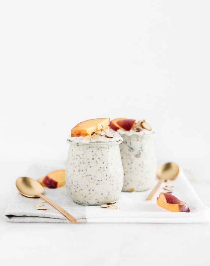 peach overnight oats in 2 glass jars with spoons beside them on a white and grey napkin.