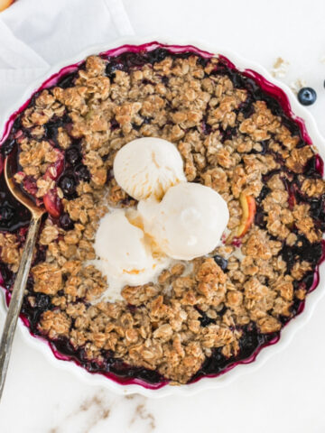 overhead view of blueberry peach crumble in a white dish with ice cream on top.