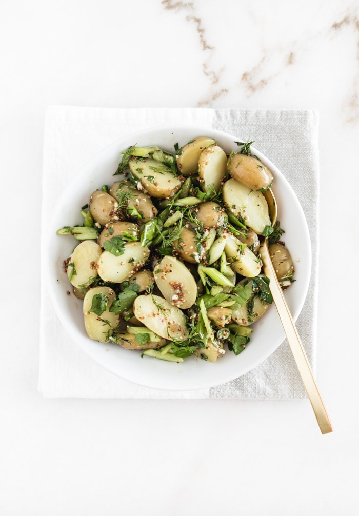 french style potato salad in a white bowl with a gold spoon in it. 