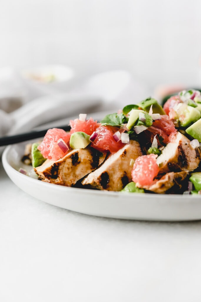 closeup of sliced grilled chicken with grapefruit avocado salsa on top.