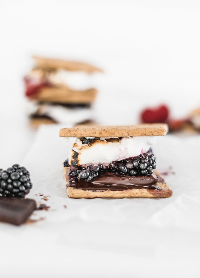 a dark chocolate berry s'more with melted chocolate and blackberries with stacked s'mores in the background