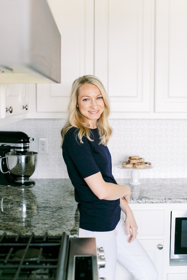 woman leaning against kitchen counter in navy shirt and white pants