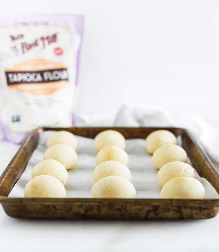 baked pan de queso rolls on a baking sheet with a bag of tapioca flour in the background