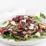 grilled pork chops on top of arugula with grilled plums and parmesan on top, on a white plate.