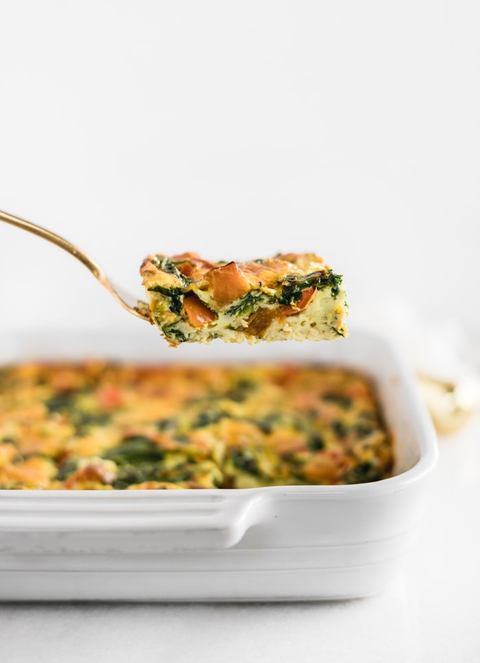 square of sweet potato breakfast casserole being lifted from a white dish with a gold serving fork