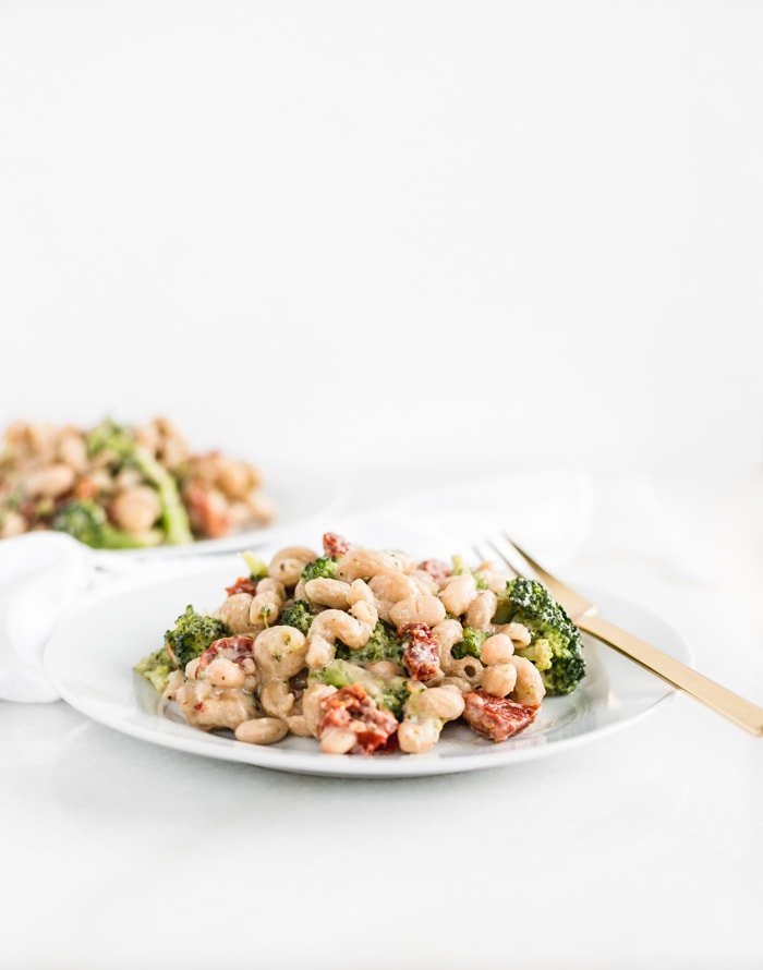 broccoli sundried tomato white bean pasta on a white plate with a gold fork