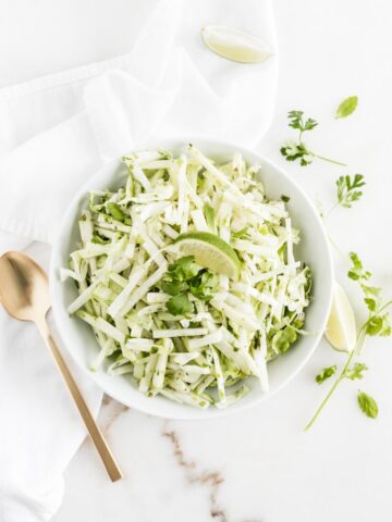 overhead shot of green apple jicama slaw with a lime wedge on top in a white bowl.