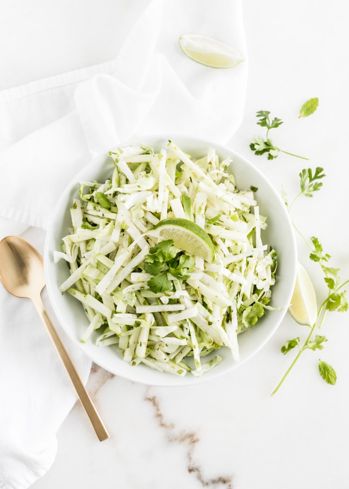 overhead shot of green apple jicama slaw with a lime wedge on top in a white bowl.